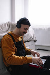 Man wearing headphones using piano at home - ASGF02259