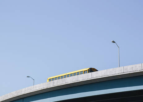 Ein gelber Schulbus fährt über eine erhöhte Fahrbahn vor einem blauen Himmel. - MINF16501