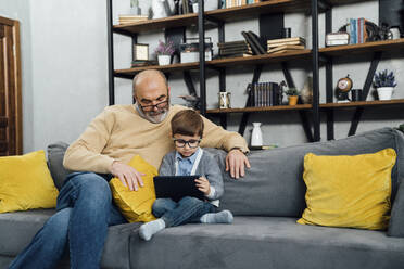 Senior man looking at grandson e-learning through tablet PC sitting on sofa in living room - VPIF05627