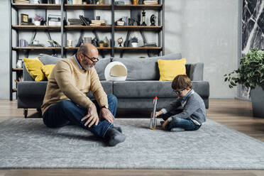 Grandfather looking at son playing with toy rocket in living room at home - VPIF05632