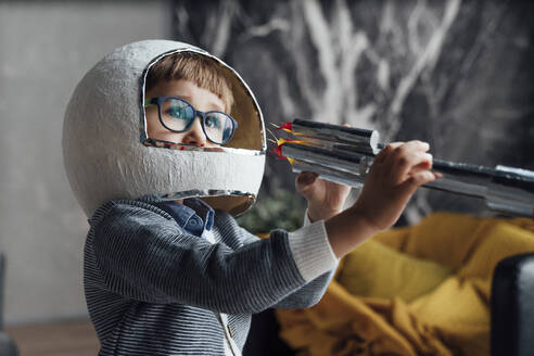 Junge mit Weltraumhelm spielt zu Hause mit einer Spielzeugrakete - VPIF05638