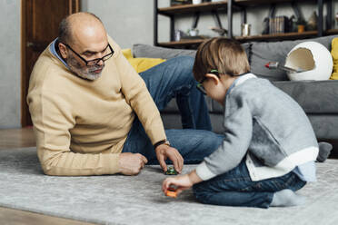 Älterer Mann und Enkel spielen mit Spielzeugauto im Wohnzimmer zu Hause - VPIF05639