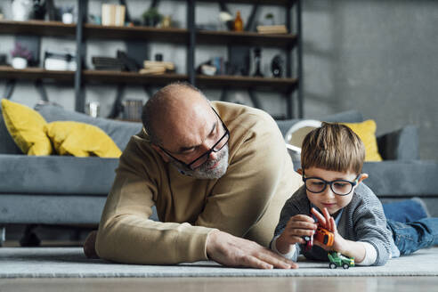 Älterer Mann sieht seinen Enkel an, der mit einem Spielzeugauto im Wohnzimmer spielt - VPIF05641