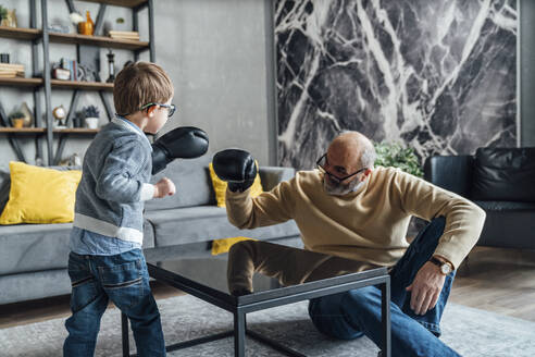 Verspielter Großvater und Enkel mit Boxhandschuh spielen im Wohnzimmer zu Hause - VPIF05648