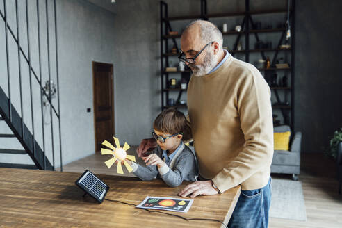 Cute boy holding model of sun by grandfather standing at table - VPIF05651