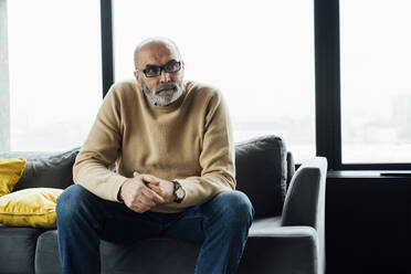 Thoughtful senior man sitting on sofa at home - VPIF05656