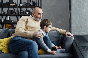 Senior man with grandson sitting on sofa in living room at home - VPIF05661