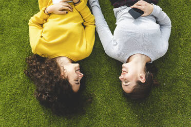 Happy young friends lying on grass at park - WPEF05946