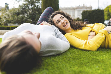 Fröhliche junge Frau, die sich mit einem Freund im Park hinlegt - WPEF05947