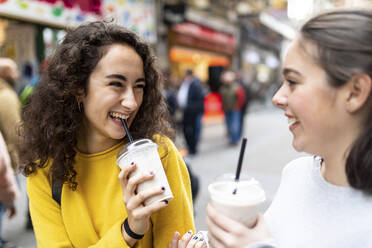 Happy young woman looking at friend drinking milkshake - WPEF05952