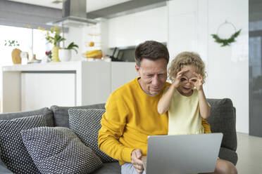 Man using laptop sitting with playful daughter in living room at home - SVKF00091