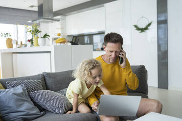 Mädchen, das einen Laptop benutzt, während der Vater mit dem Handy im Wohnzimmer telefoniert - SVKF00099