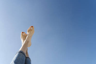 Woman with crossed barefeet under clear blue sky - CHPF00847