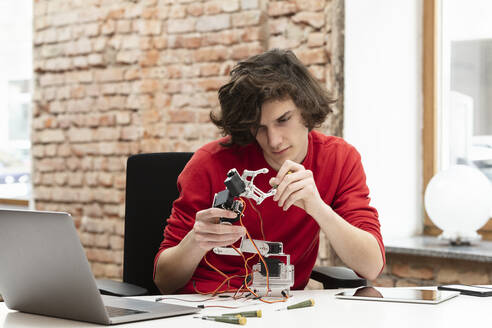 Jugendlicher arbeitet an einem kleinen Roboterarm, der mit einem Laptop am Tisch sitzt - DHEF00646