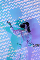 Frau in Freizeitkleidung und moderner schwarzer VR-Brille mit verschiedenen projizierten Zahlen beim Erkunden des Cyberspace in einem Raum - ADSF34522
