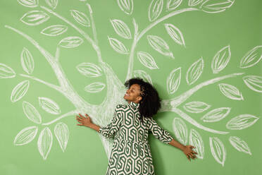 Lächelnde Frau mit geschlossenen Augen umarmt Baum Zeichnung auf grüne Wand - EIF03884