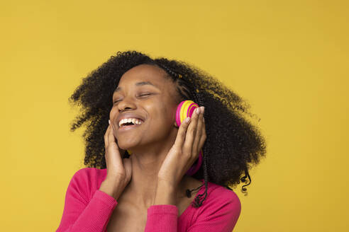Glückliche junge Frau mit geschlossenen Augen, die Musik über drahtlose Kopfhörer vor gelbem Hintergrund genießt - EIF03900
