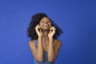 Young woman with eyes closed laughing against blue background - EIF03907