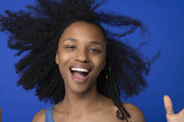 Happy young woman with mouth open against blue background - EIF03909