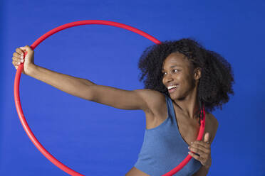 Happy young woman with red hoop against blue background - EIF03917