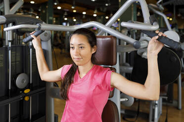 Junge Frau beim Training mit Fitnessgeräten im Fitnessstudio - IFRF01569