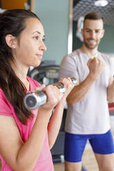 Instructor motivating woman exercising with dumbbells at gym - IFRF01573