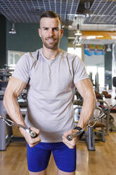 Lächelnder junger Mann beim Training im Fitnessstudio - IFRF01588