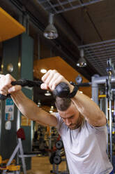 Mann trainiert an einer Kabelmaschine im Fitnessstudio - IFRF01594