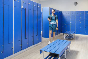 Young man with backpack walking in locker room at gym - IFRF01598