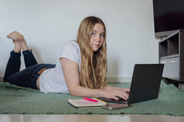 Young woman lying with laptop at home - PGF01069