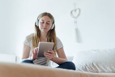 Junge Frau hört Musik über Kopfhörer mit einem Tablet-PC, der zu Hause auf dem Bett steht - PGF01072