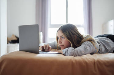 Junge Frau mit Laptop auf dem Bett liegend zu Hause - PGF01075
