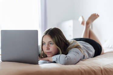 Junge Frau mit Laptop auf dem Bett liegend zu Hause - PGF01077