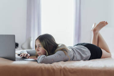 Frau mit Laptop auf dem Bett liegend zu Hause - PGF01078