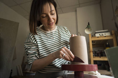 Woman shaping ceramics with hand tool at workshop - SSGF00696