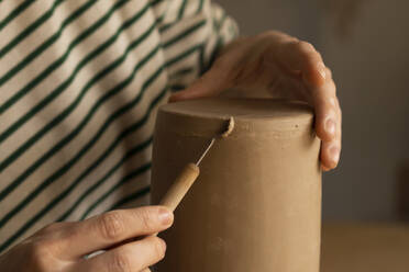Hands of woman shaping clay with hand tool at workshop - SSGF00697