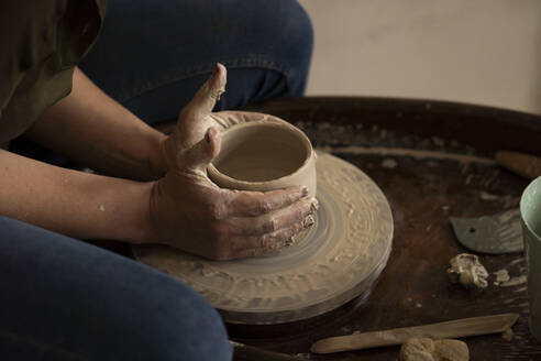 Craftsperson making pot with clay on pottery wheel at workshop - SSGF00703