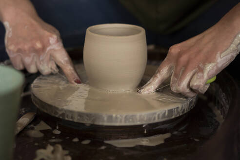 Woman cutting clay on pottery wheel with thread at workshop - SSGF00704