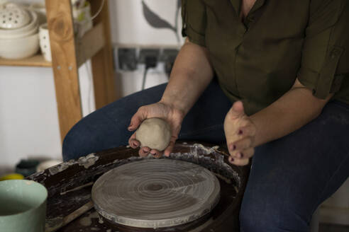 Woman molding clay dough sitting by pottery wheel at workshop - SSGF00705