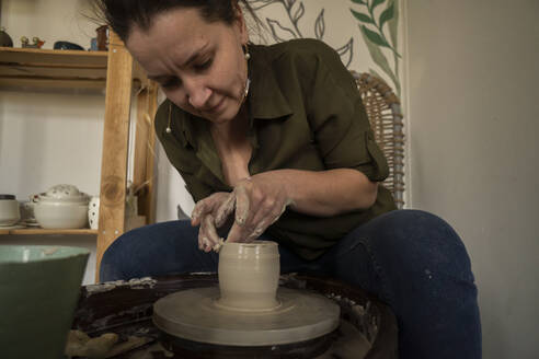 Woman making clay pot on pottery wheel at workshop - SSGF00706