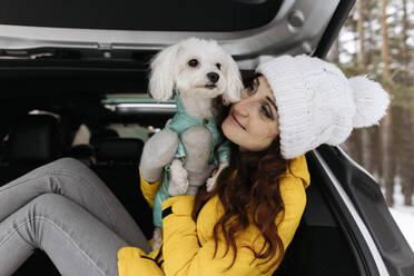 Smiling redhead woman embracing dog sitting in car trunk - SIF00069