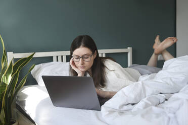 Frau mit Laptop auf dem Bett liegend zu Hause - VBUF00082