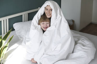 Glückliche Mutter und Sohn, eingewickelt in eine Decke, sitzen zu Hause auf dem Bett - VBUF00089