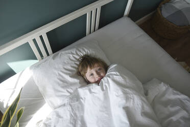 Cute boy with blanket lying in bed at home - VBUF00091