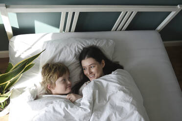 Mutter und Sohn mit Decke im Bett liegend zu Hause - VBUF00093