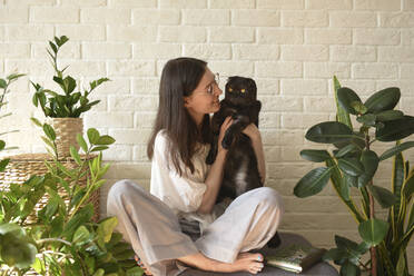 Smiling woman with cat sitting cross-legged on seat at home - VBUF00102