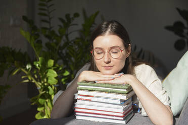 Frau mit geschlossenen Augen, die sich zu Hause auf Bücher stützt - VBUF00120
