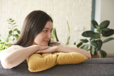 Lächelnde Frau mit gelbem Kissen sitzt zu Hause auf dem Sofa - VBUF00124