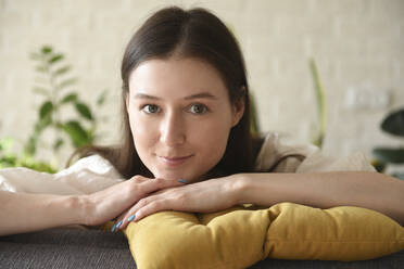Lächelnde Frau mit gelbem Kissen sitzt zu Hause - VBUF00125