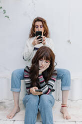 Gelangweilte Frau, die ihr Smartphone vor einem Freund benutzt, der ihr im Hinterhof eine SMS schickt - MRRF01983